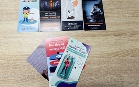 bi&oacute;r kolorowych ulotek profilaktycznych dla dzieci i młodzieży ułożonych na jasnym, drewnianym blacie. W g&oacute;rnym rzędzie leżą cztery pionowe broszury o tematyce bezpieczeństwa na drodze, szkodliwości e-papieros&oacute;w, przeciwdziałania alkoholizmowi oraz cyberp