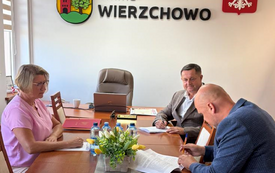 Zdjęcie przedstawia oficjalne spotkanie w urzędzie gminy, o czym świadczy umieszczone na ścianie godło Polski oraz napis &bdquo;Gmina Wierzchowo"